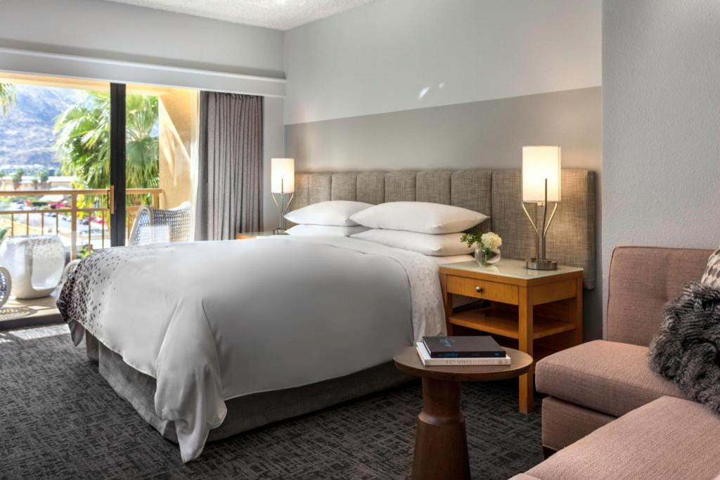 A hotel in Palm Springs California with a cozy bed, side table, lamp and couch.