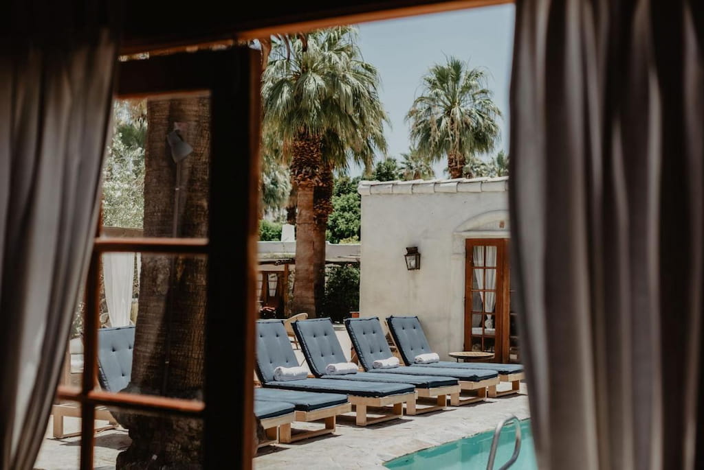 best boutique hotels in Palm Springs California with blue cushioned pool loungers through airy curtains and palm trees