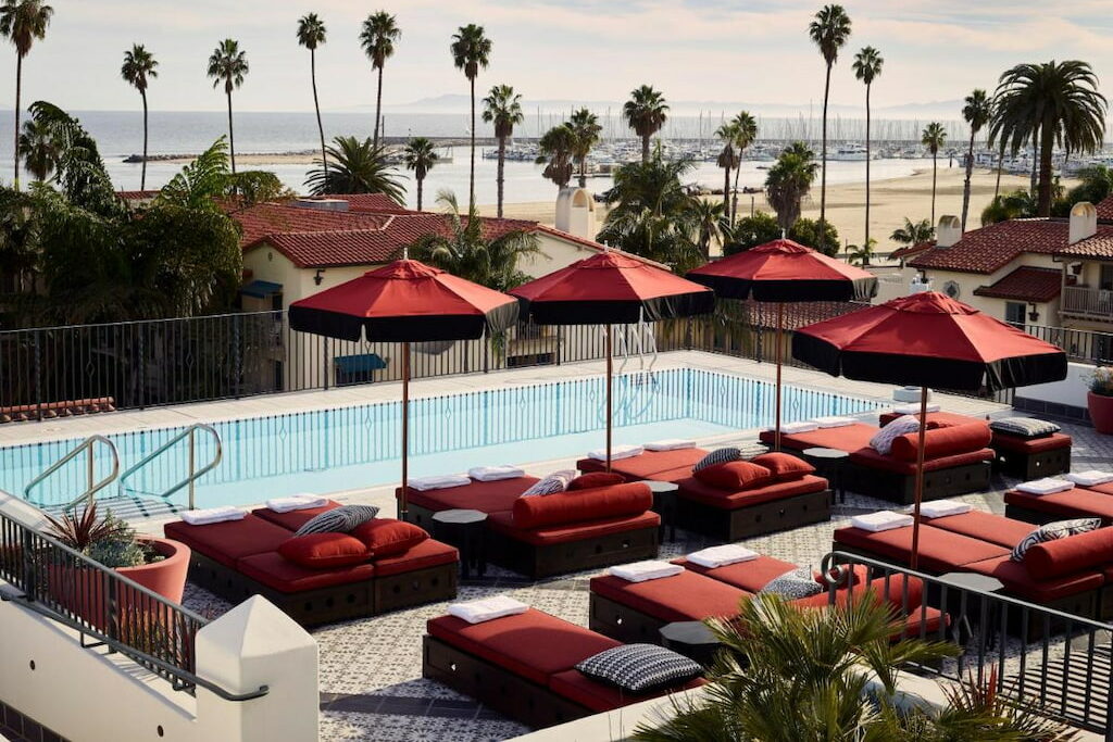 An outdoor pool surrounded by maroon pool benches and umbrellas.
