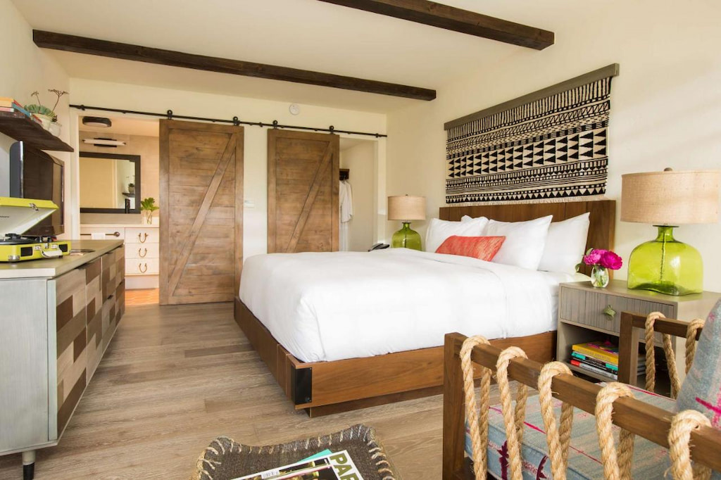 A room with a wooden sliding door near the bed with white linens, side table and drawers.