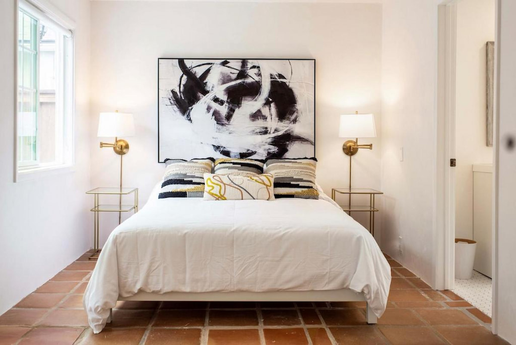 A cozy bed below a huge painting in an all white room.