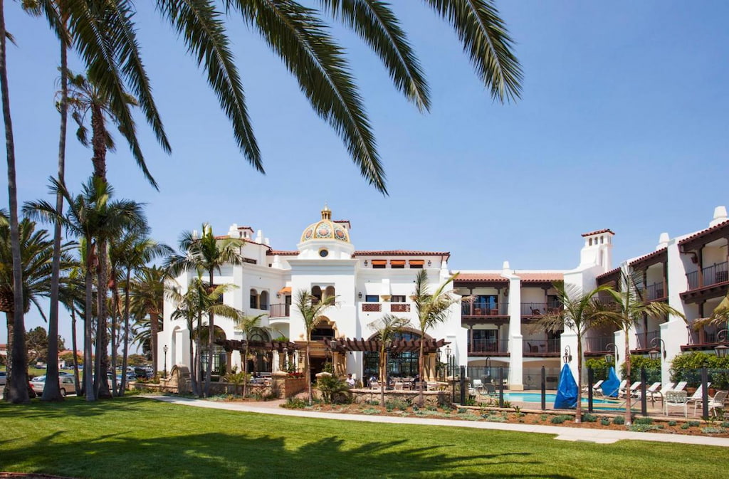 white painted best Santa Barbara boutique hotels sit in the distance with green lawn and palm tree on a sunny blue day