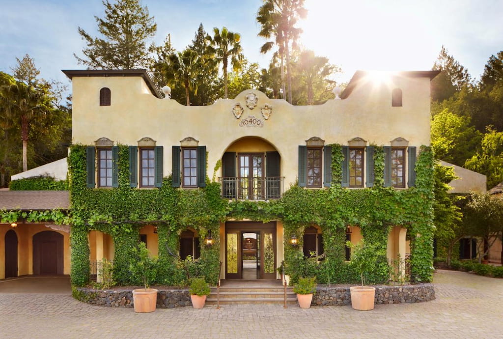 Hotel exterior with creme colored and ivy covered walls with wood framed windows and arched door way
