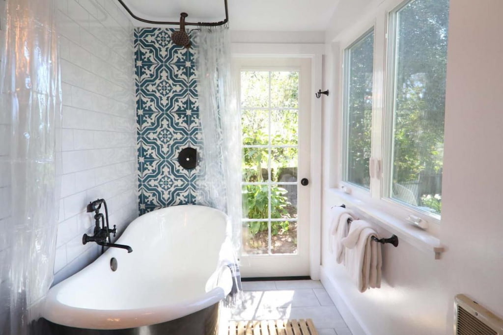 historic bathroom with vintage-style clawfoot tub near the window with a blue and white patterned feature wall and plenty of natural light