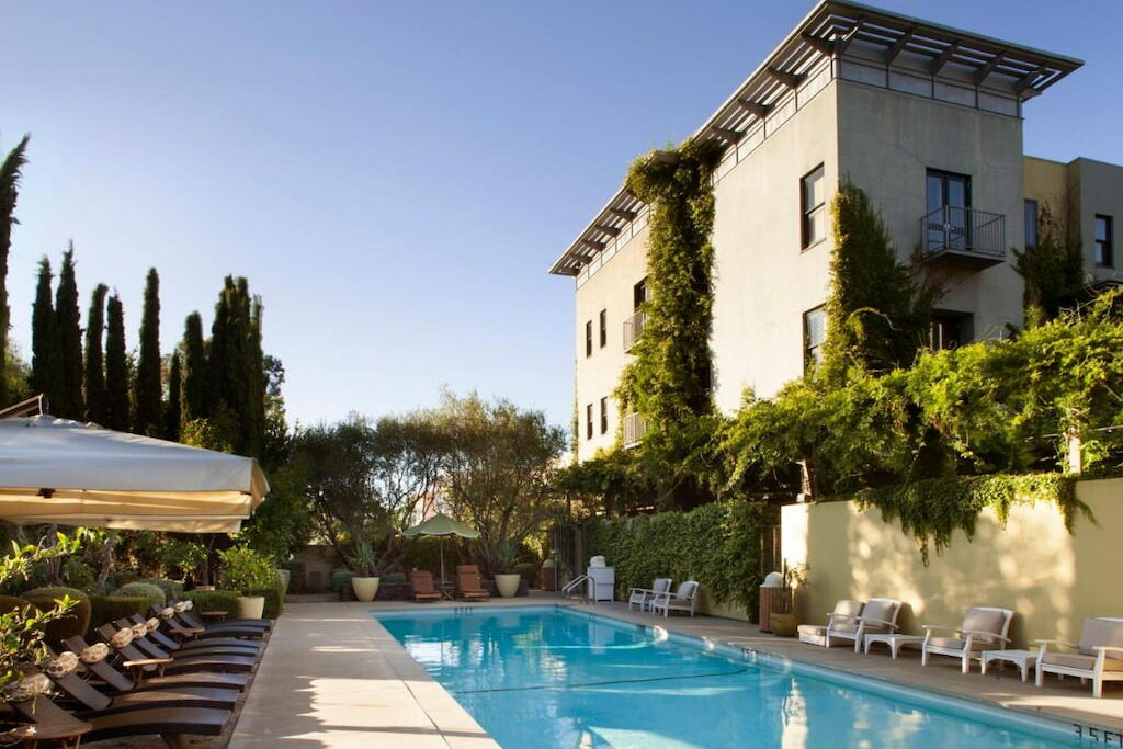 outdoor pool area with wooden loungers and large pool umbrellas sit before a tall ivy covered Sonoma Valley CA hotel