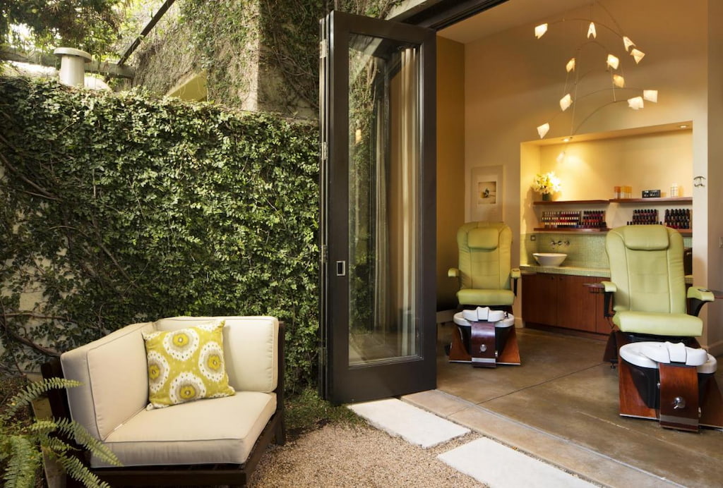 outside looking into a spa area with greenery covering the external wall with a white cushioned chair underneath