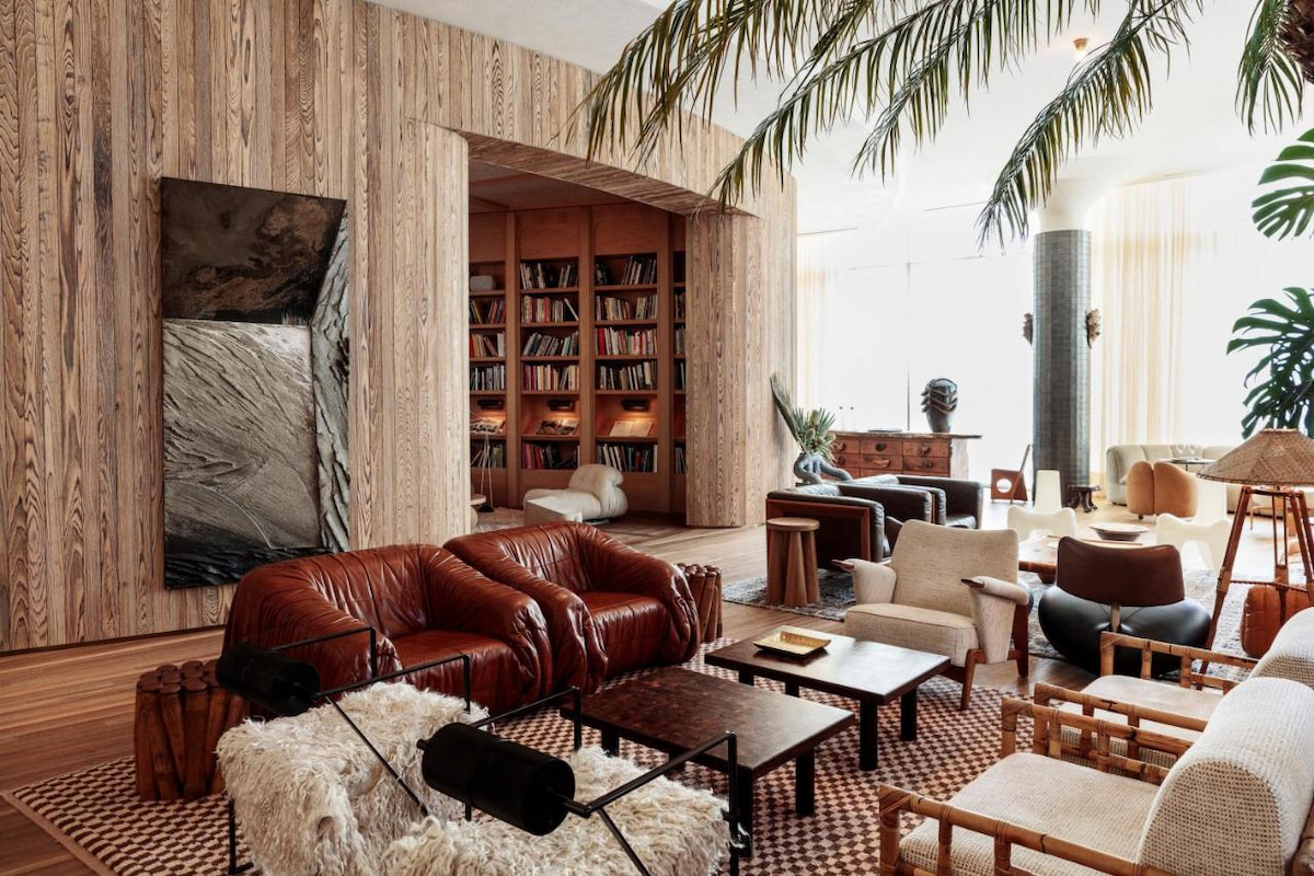 A room in one of the best boutique hotels in Southern California with brown, wooden interiors, bookshelves, indoor plants, and various tables and chairs