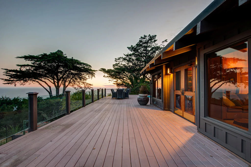 Best Boutique Hotels in Big Sur California at sunset with wood slatted balcony and lit up interior of a single story house on the right with tree on the left