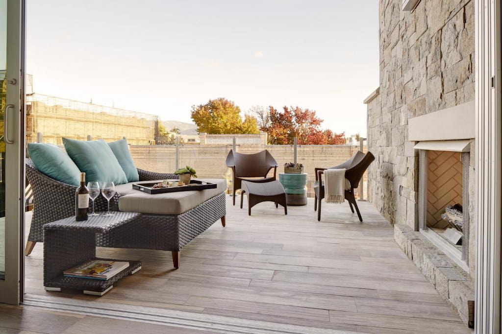 an outdoor common area with a couple of padded sofa chairs in fornt of the fireplace.
