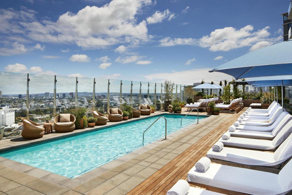 A rooftop swimming pool surrounded by padded pool benches and umbrellas under a sunny day.