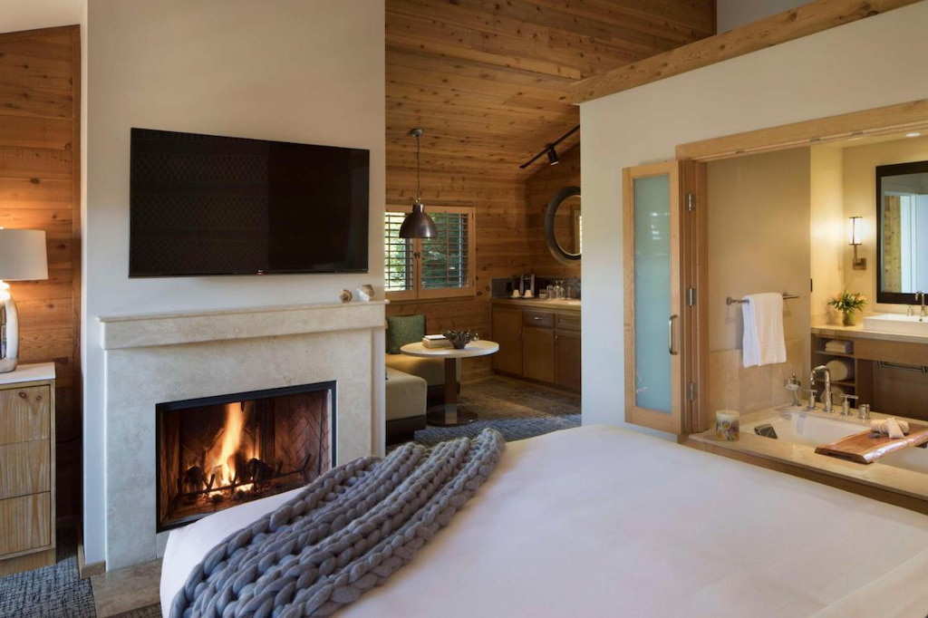 View of a spacious bedroom with a kingsize bed with white sheets near the fireplace.