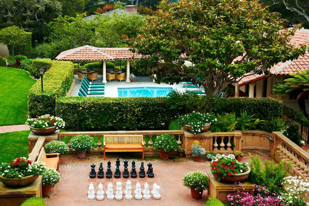 An outdoor area with swimming pool, trees, plants, flowers, and life-size chess set
