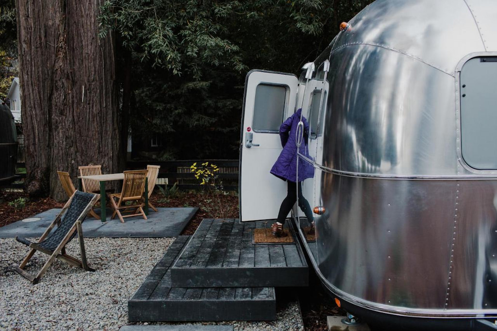 vintage AirStream camper with black wood patio and outdoor chairs with a dark green forest in the background at a resort in Russian River Valley CA