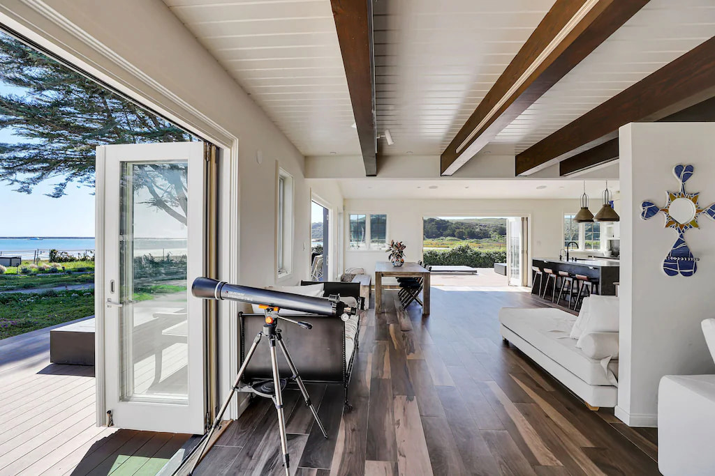 A luxury vacation home in Half Moon Bay with elegant furniture and telescope pointing out to the open doors, patio and coastline