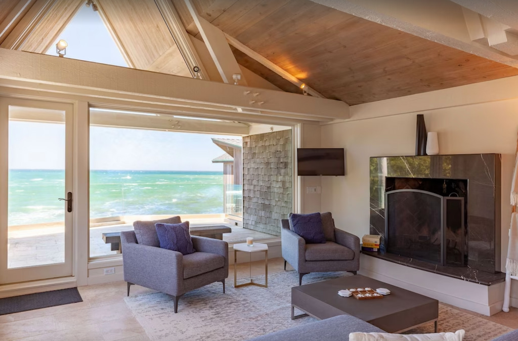 A fireplace near the accent chairs and a ceiling-to-floor windows and door with view of the beach.