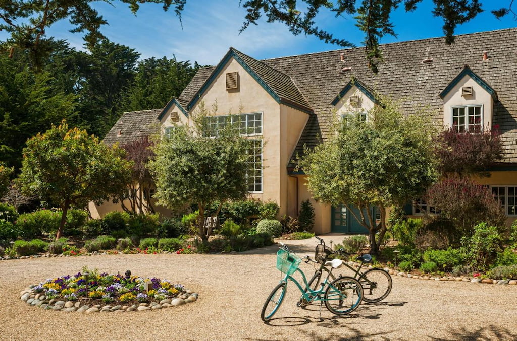 A country-style building surrounded by small trees and and green plants and a flower bed and a couple of bicycles parked in front.