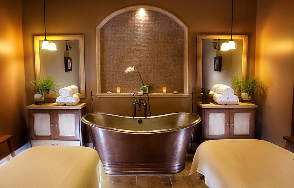A metal bathtub in the middle of the room with two vanity mirrors with a multiple rolled white towels.