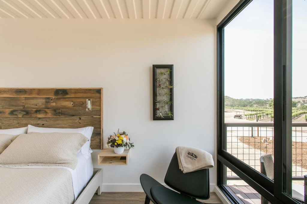 modern all white painted winery hotel in Paso Robles with black accent chair and wood headboard by a black framed window
