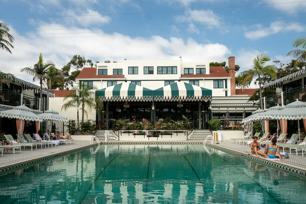 large outdoor pool surrounded by stripped pool umbrellas and canopy on a partly cloudy day at a hip hotel in San Diego CA