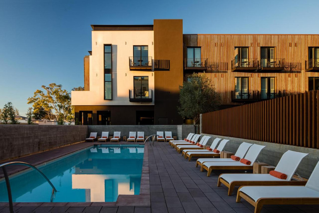 a modern two story downtown San Luis Obispo hotel sits behind a rectangular outdoor pool with white sun loungers at dawn