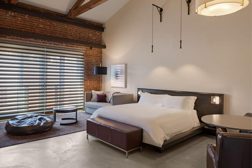 sleek San Luis Obispo hotel suite with red brick feature wall, low lying bed and brown leather furniture