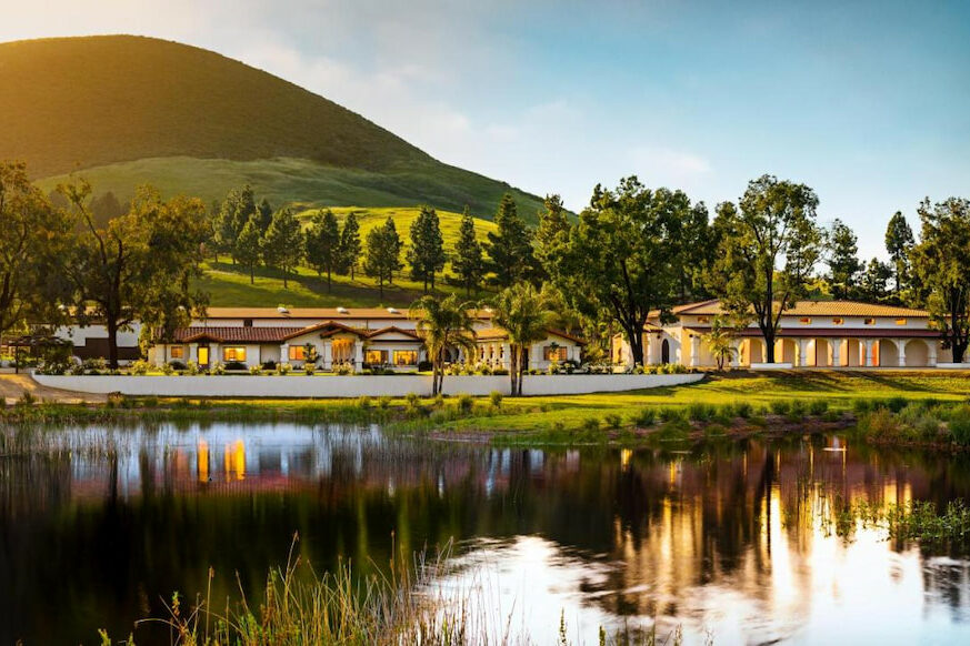 a reflection on a lake of a luxury hotel in San Luis Obispo wine country with rolling green hills on a blue sunny day