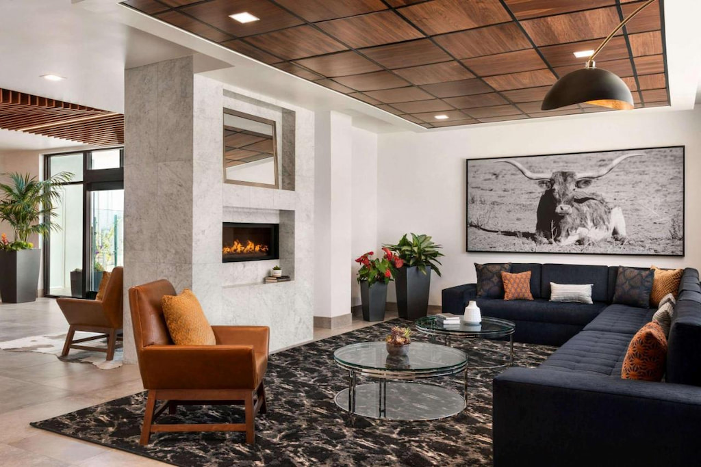 a cozy modern hotel lobby with black and white artwork of a yak, white marble fireplace, brown leather lounge chair and large black sectional with wood ceiling