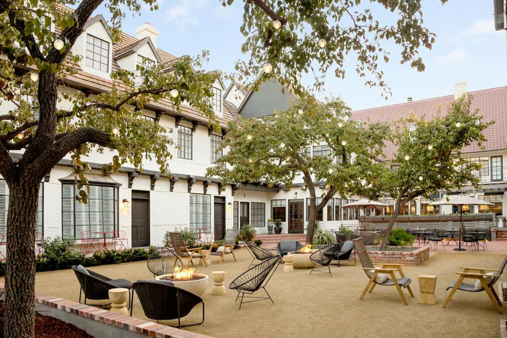 spacious outdoor courtyard with lounge furniture, two story white painted boutique Solvang hotel with tall trees