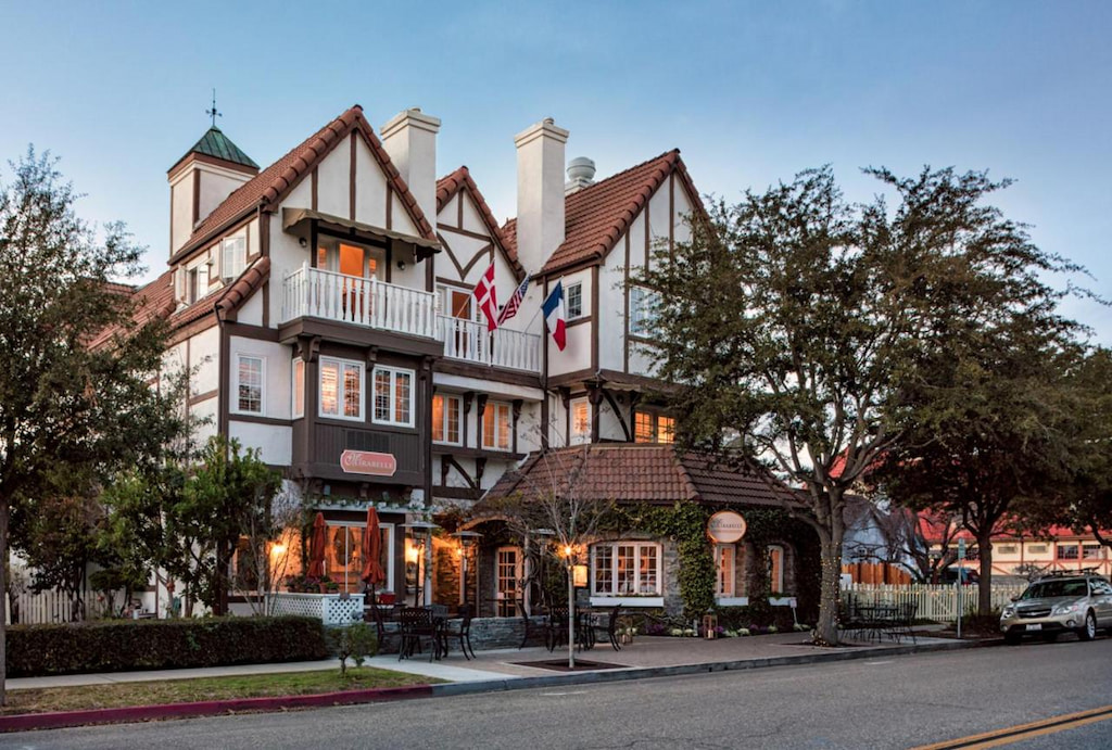 victorian exterior facade of a historic hotel in downtown Solvang with brown tiled roof and trees on the roadway
