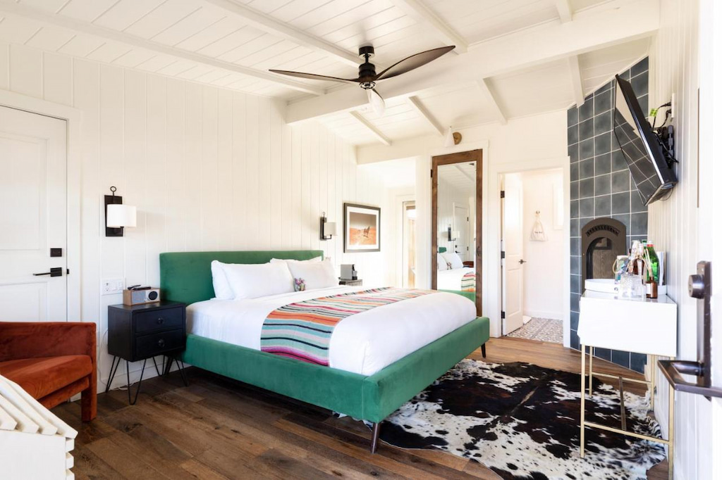 retro-chic hotel room with green framed bed, grey tiled fireplace, red chair and vintage sink
