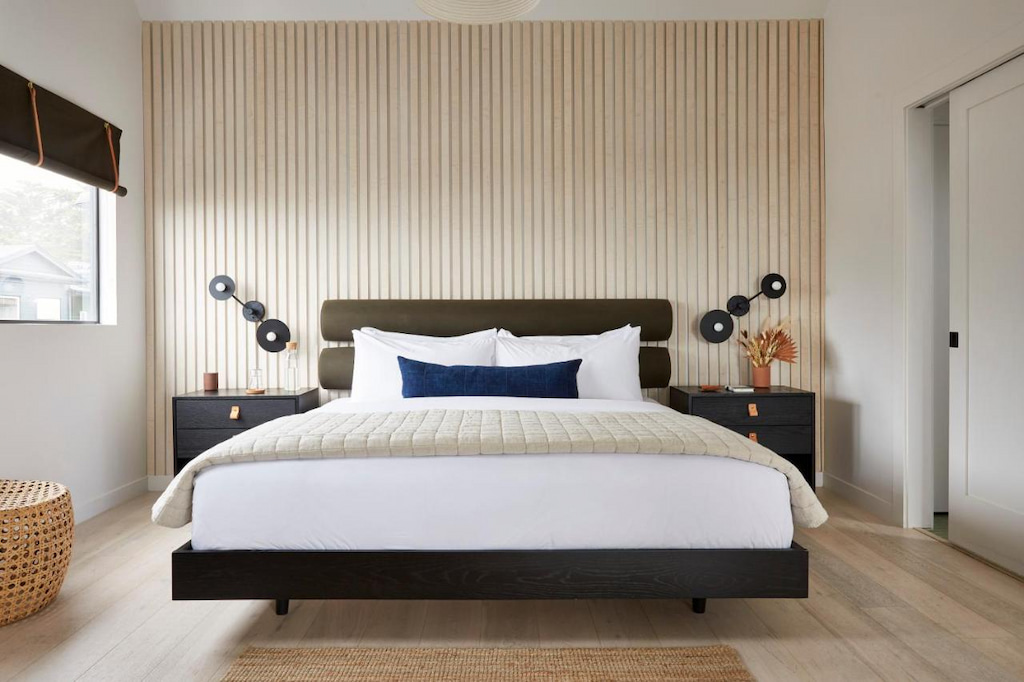 slatted wooden accent wall in an elegant hotel room with white linens and wood floor